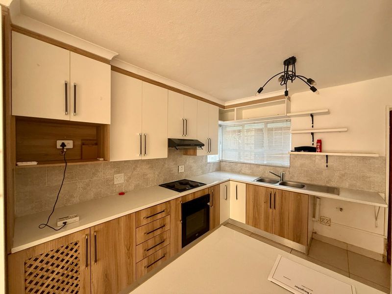 A clean and functional kitchen featuring modern wood-grain and white cabinetry, integrated appliances, a double sink, and neutral tiled backsplash.