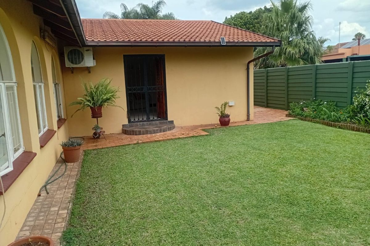 A well-maintained rear garden featuring a paved patio area, lawn, and secure access to the home with an installed air conditioning unit.