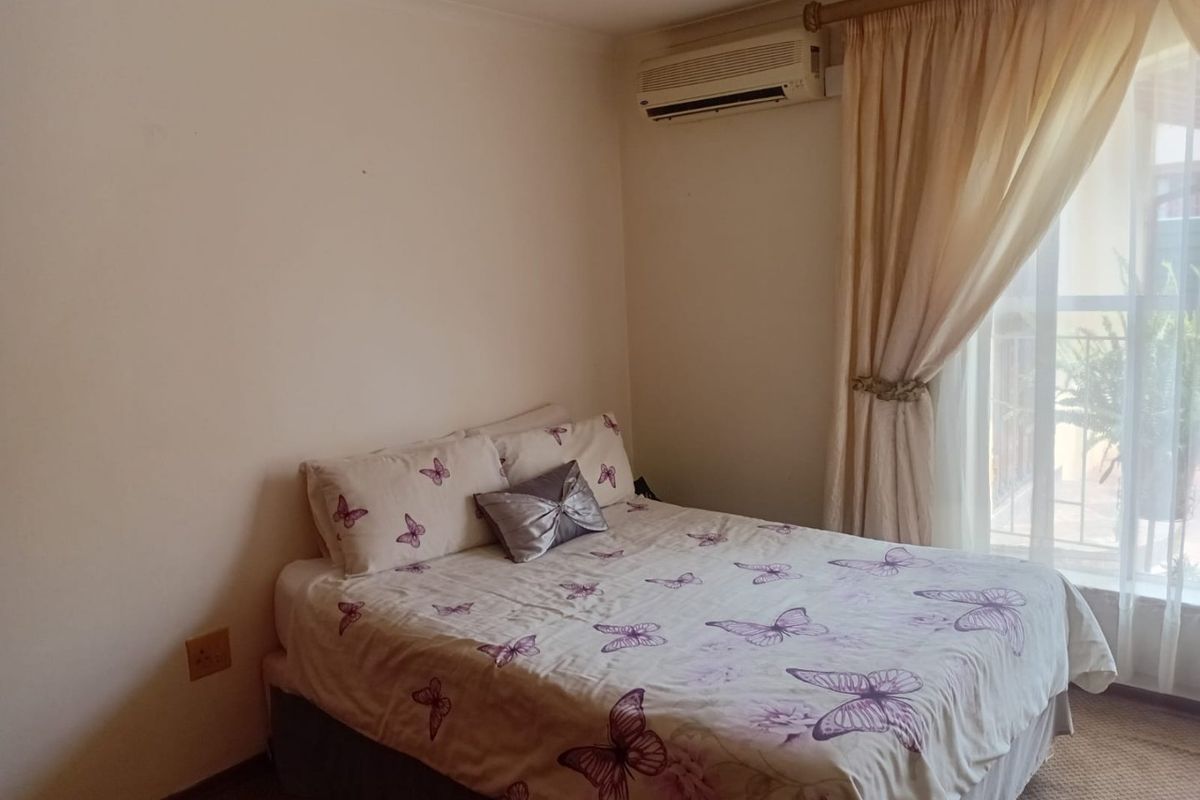 A functional bedroom featuring a wall-mounted air conditioning unit, recessed lighting, and a sliding glass door providing access to an outdoor area.