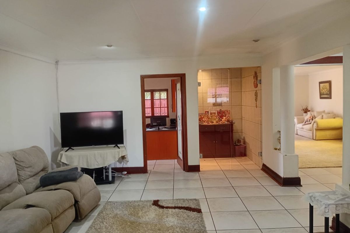 Spacious living area featuring neutral tiled flooring, recessed lighting, and an open-plan layout connecting to adjacent rooms through a glass partition and archway.