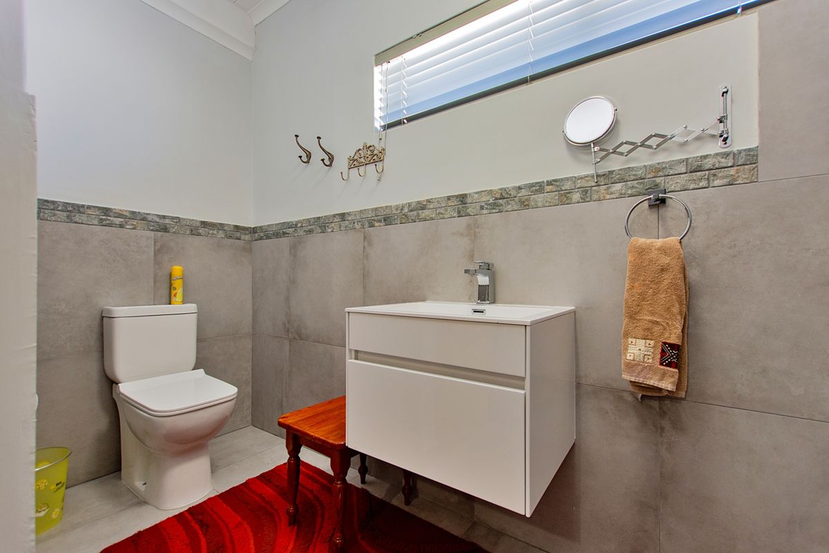 A modern bathroom featuring a wall-mounted vanity, ceramic toilet, and neutral large-format wall tiles with a decorative mosaic border.