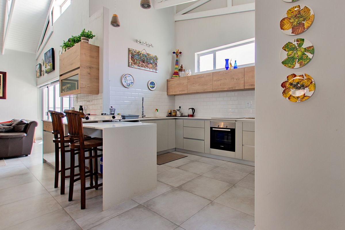 Modern kitchen featuring light-toned cabinetry, stone countertops, subway tile backsplash, and a breakfast island, set under high ceilings with exposed trusses.