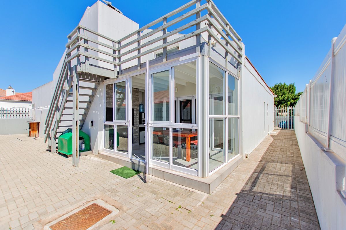 Rear exterior view of the property featuring a paved courtyard, external staircase leading to a balcony, and modern sliding glass doors.