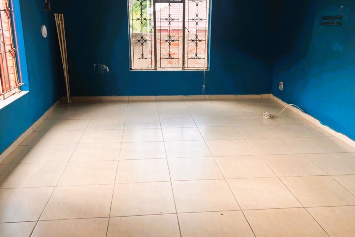 An empty living room featuring tiled flooring and security bars on the windows, presenting a blank canvas for potential interior design updates.