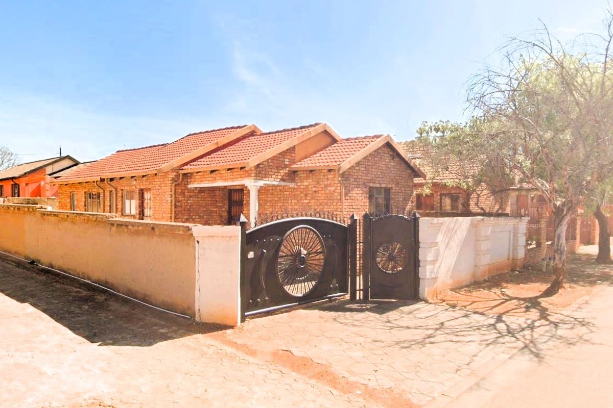A single-story face-brick house featuring a tiled roof, secure perimeter wall, and decorative metal driveway gate.