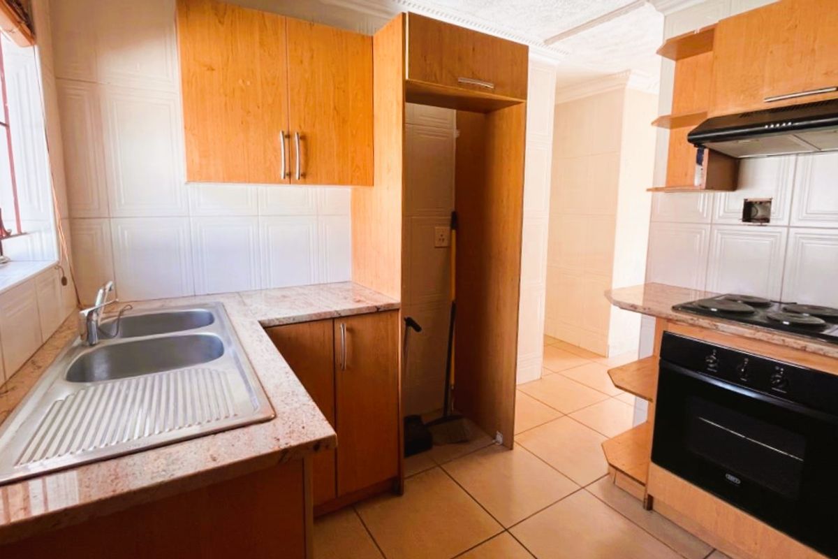 Functional kitchen featuring light wood cabinetry, granite-look countertops, built-in oven, hob, extractor fan, and a double stainless steel sink.