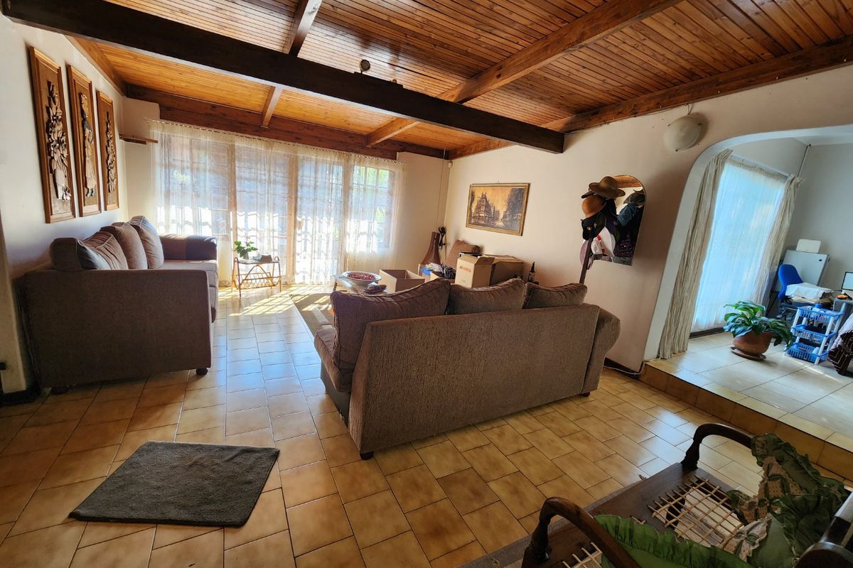 Spacious living room featuring a rustic exposed timber beam ceiling, ceramic tiled flooring, and large sliding glass doors providing natural light.