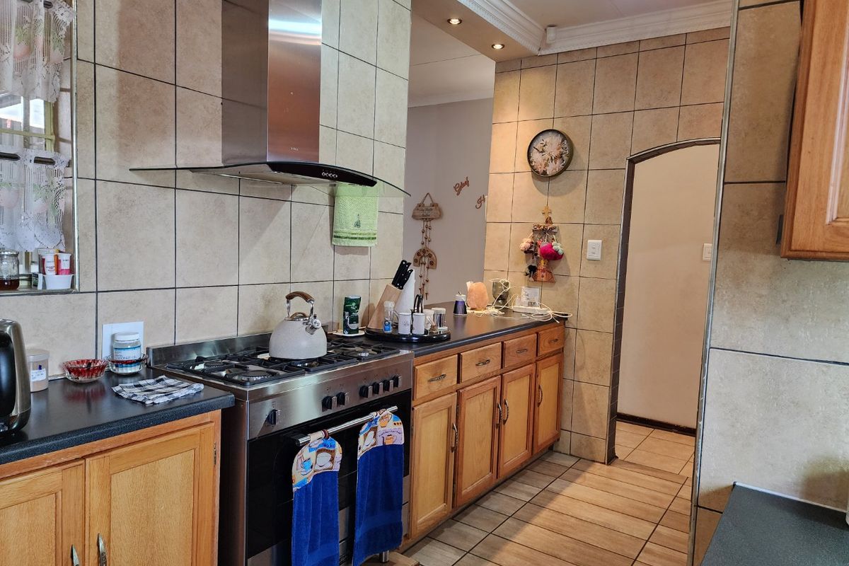 A functional kitchen featuring wooden cabinetry, tiled splashbacks, a stainless steel gas stove with extractor fan, and tiled flooring.