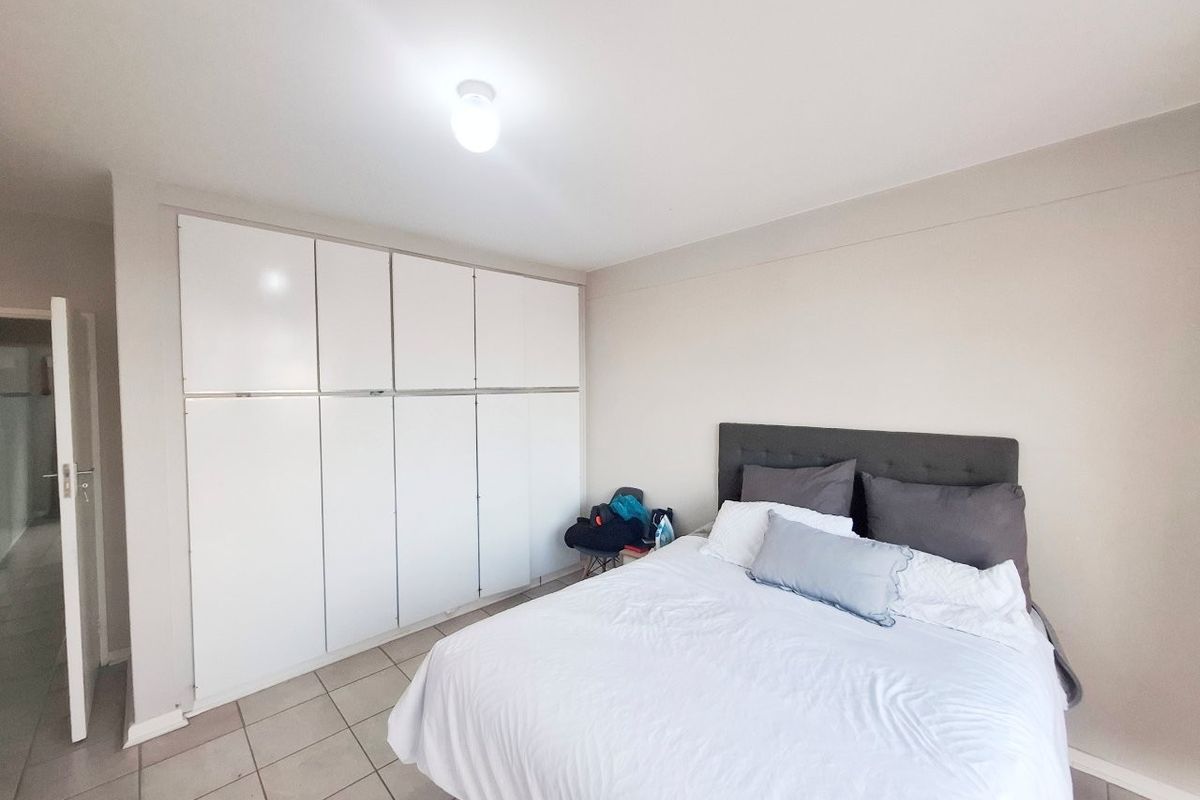A well-lit bedroom featuring neutral walls, tiled flooring, and extensive floor-to-ceiling built-in cupboards providing ample storage space.