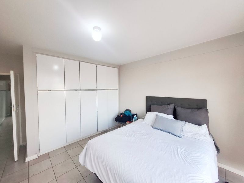 A well-lit bedroom featuring neutral walls, tiled flooring, and extensive floor-to-ceiling built-in cupboards providing ample storage space.