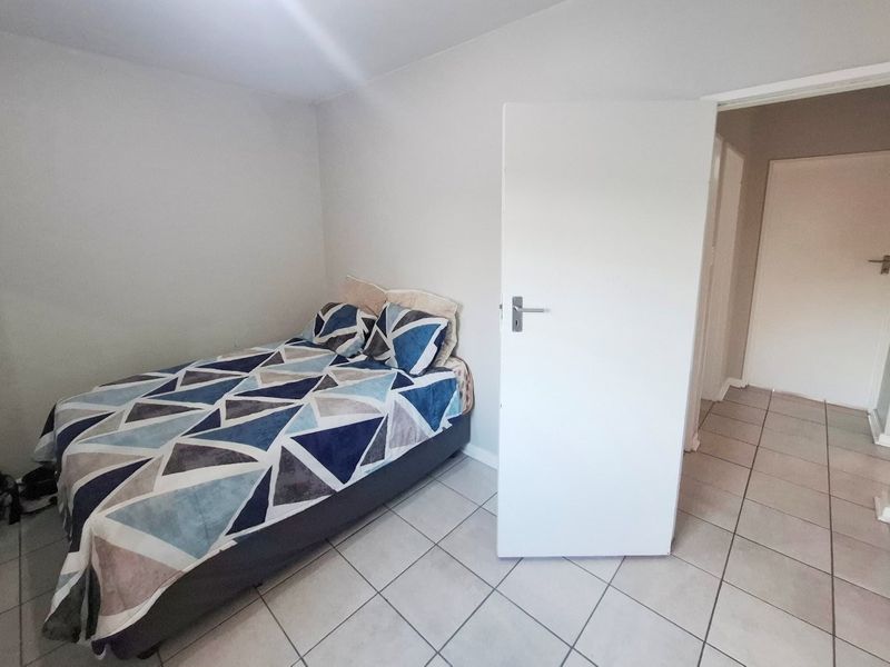A simple bedroom featuring neutral wall finishes and tiled flooring, providing a functional space with direct access to the hallway.