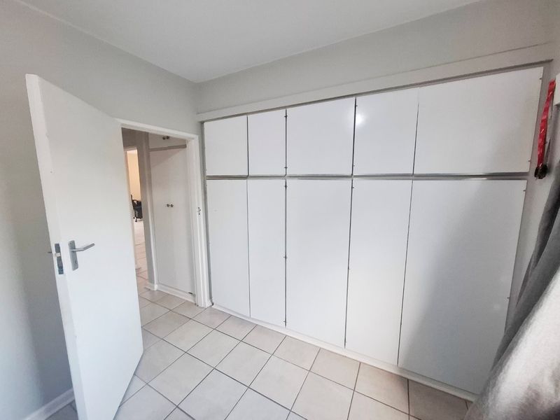 A clean, empty bedroom featuring neutral tiled flooring and extensive white built-in cupboard storage.