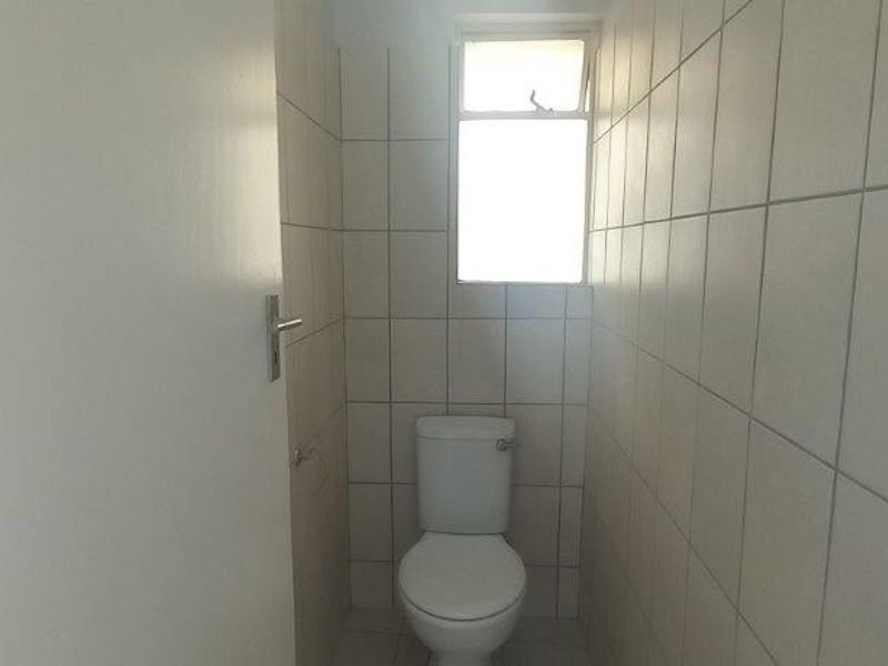A simple, functional bathroom featuring tiled walls, a standard toilet, and a window for natural light.
