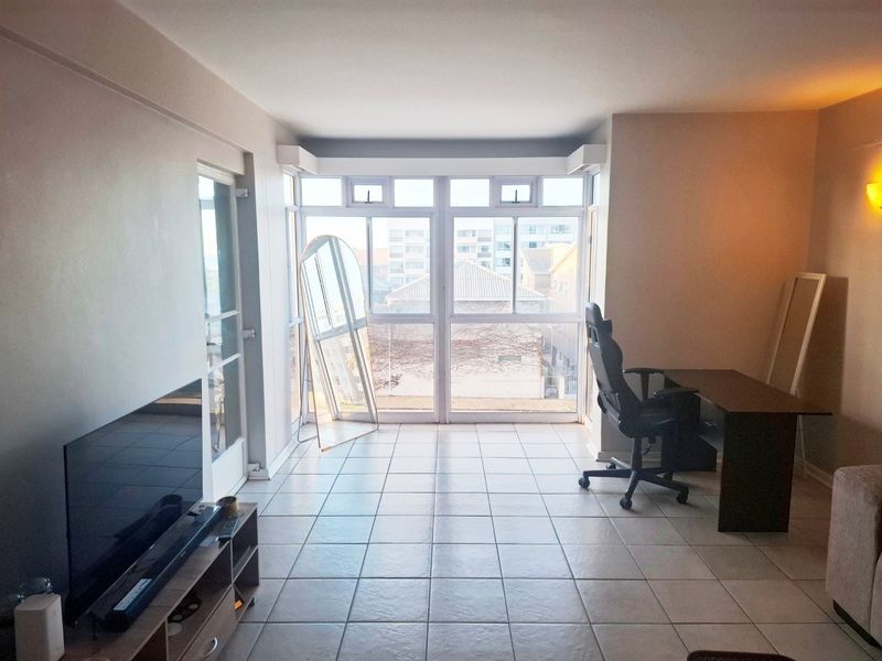 A bright living area featuring tiled flooring and large windows that provide ample natural light and an urban view.