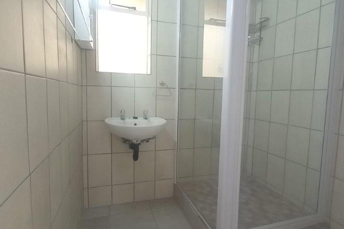 A functional bathroom featuring a wall-mounted basin, a shower enclosure with a glass door, and neutral wall and floor tiling.