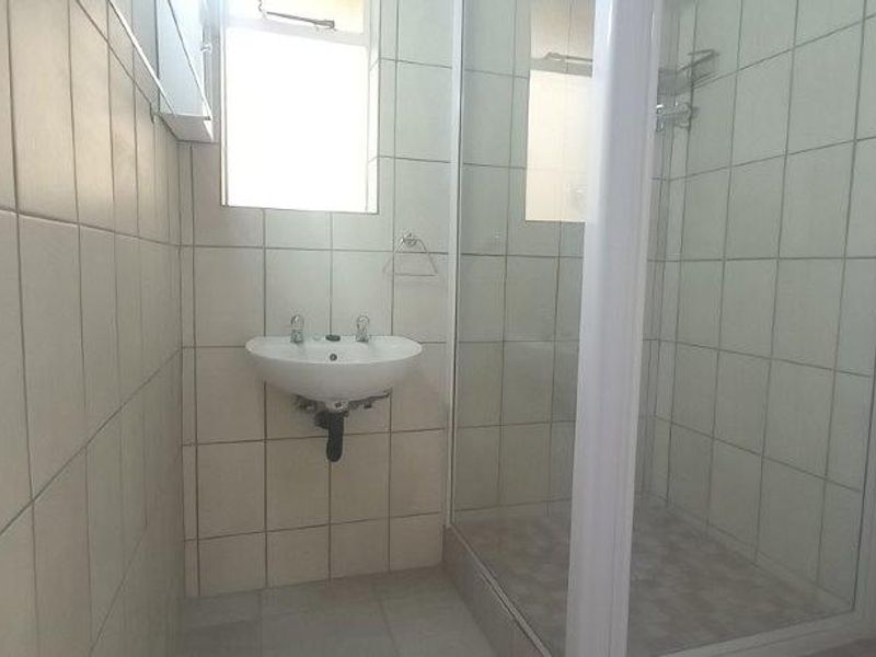 A functional bathroom featuring a wall-mounted basin, a shower enclosure with a glass door, and neutral wall and floor tiling.