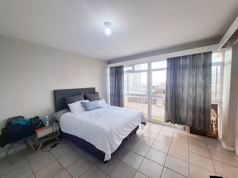 A bedroom featuring tiled flooring and large windows that provide natural light and exterior views.