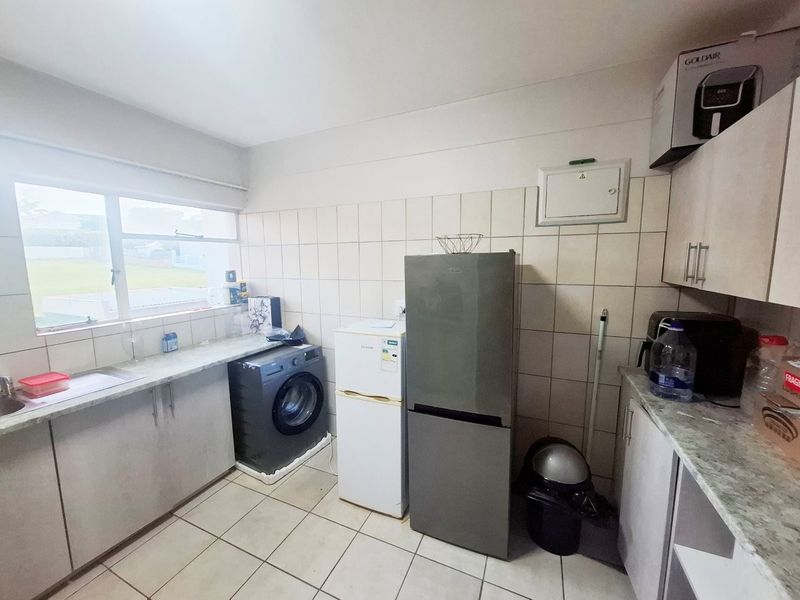 Functional kitchen featuring tiled backsplash, laminate countertops, built-in cabinetry, and tiled flooring with a window providing natural light.