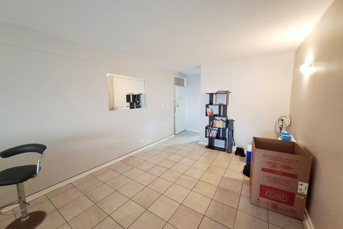 A spacious, neutrally painted living area featuring tiled flooring and a wall-mounted light fixture, offering a clean and versatile blank canvas.