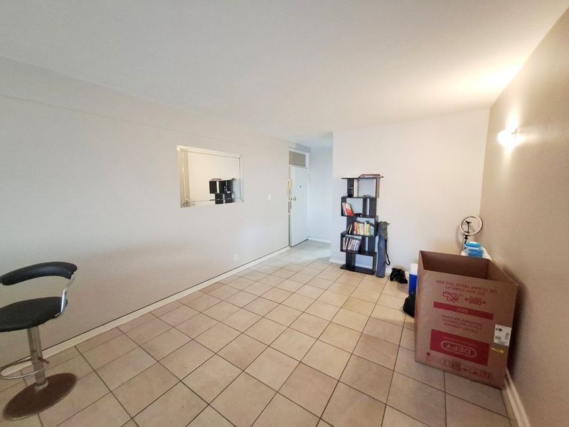 A spacious, neutrally painted living area featuring tiled flooring and a wall-mounted light fixture, offering a clean and versatile blank canvas.