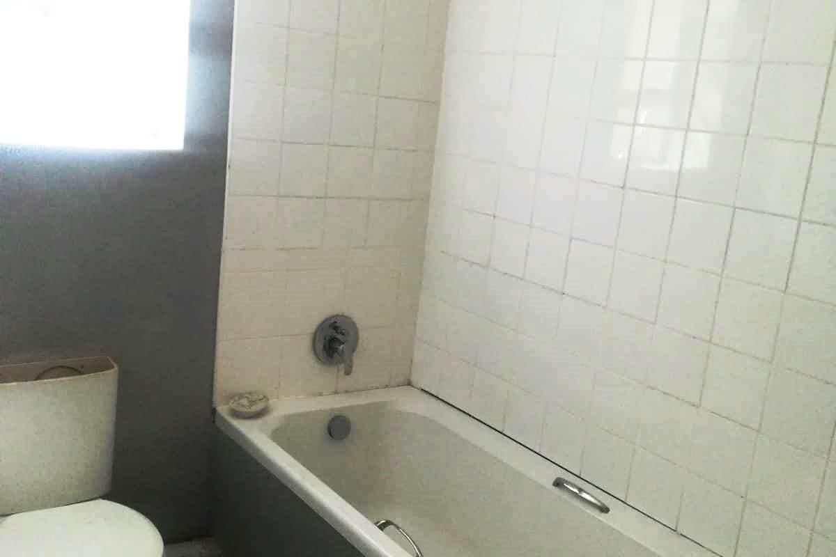 A dated bathroom featuring a standard bathtub with shower mixer and a toilet, requiring cosmetic updates to improve the overall aesthetic and condition.