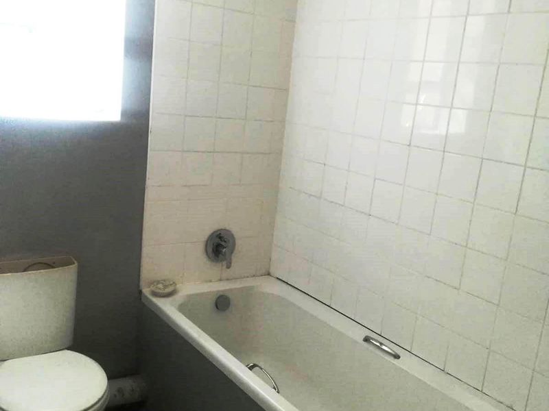 A dated bathroom featuring a standard bathtub with shower mixer and a toilet, requiring cosmetic updates to improve the overall aesthetic and condition.