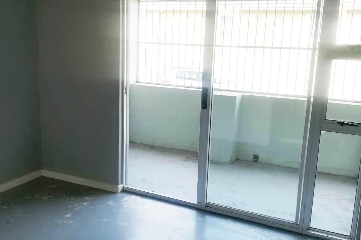 An empty living room featuring a sliding glass door with security bars and worn flooring, offering access to an outdoor balcony area.