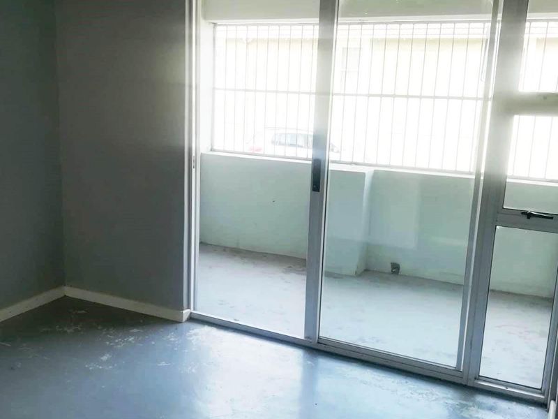 An empty living room featuring a sliding glass door with security bars and worn flooring, offering access to an outdoor balcony area.