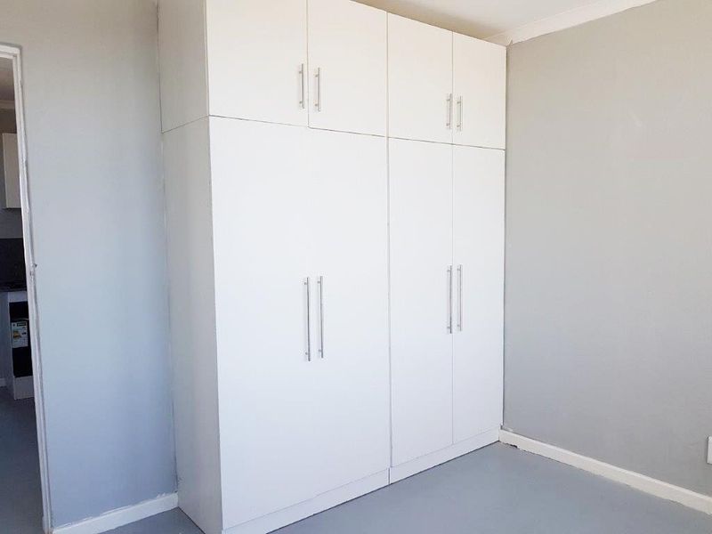 A clean, empty bedroom featuring floor-to-ceiling white built-in cupboards with modern handles and neutral grey wall finishes.