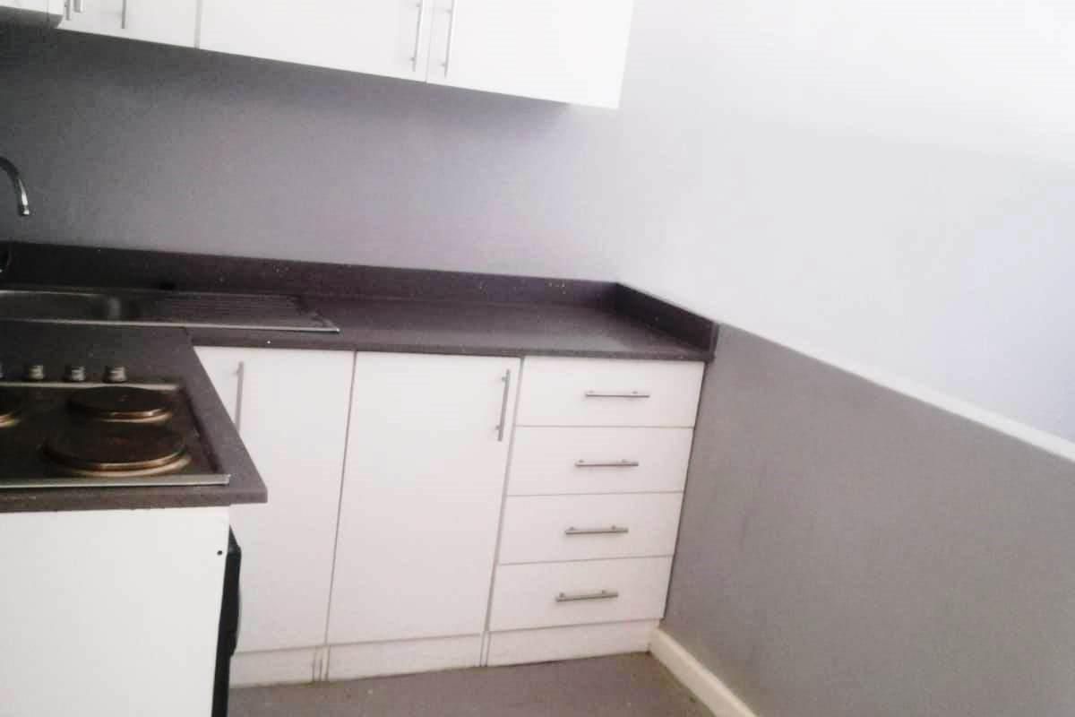 A compact kitchen featuring white cabinetry, dark countertops, and a built-in electric hob, presenting a functional space ready for updates.