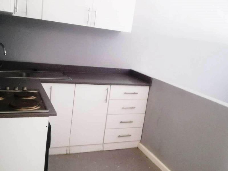 A compact kitchen featuring white cabinetry, dark countertops, and a built-in electric hob, presenting a functional space ready for updates.