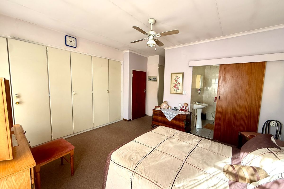 Spacious bedroom featuring extensive built-in cupboards, a ceiling fan, and an attached en-suite bathroom with a sliding door entry.