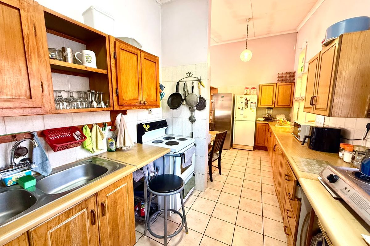 A functional kitchen featuring wooden cabinetry, laminate countertops, a stainless steel double sink, and a freestanding stove with tiled flooring and splashbacks.