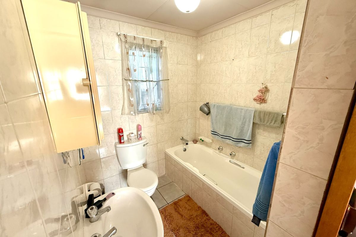 A dated bathroom featuring a standard bathtub, pedestal basin, and toilet with full-height wall tiling and tiled flooring.