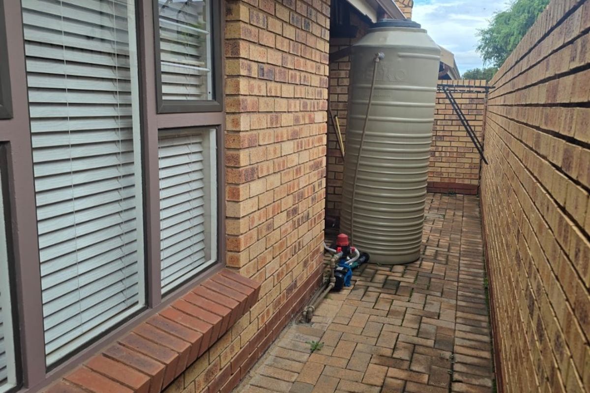 Side passage featuring brick paving, a water storage tank with pump, and brick boundary walling.