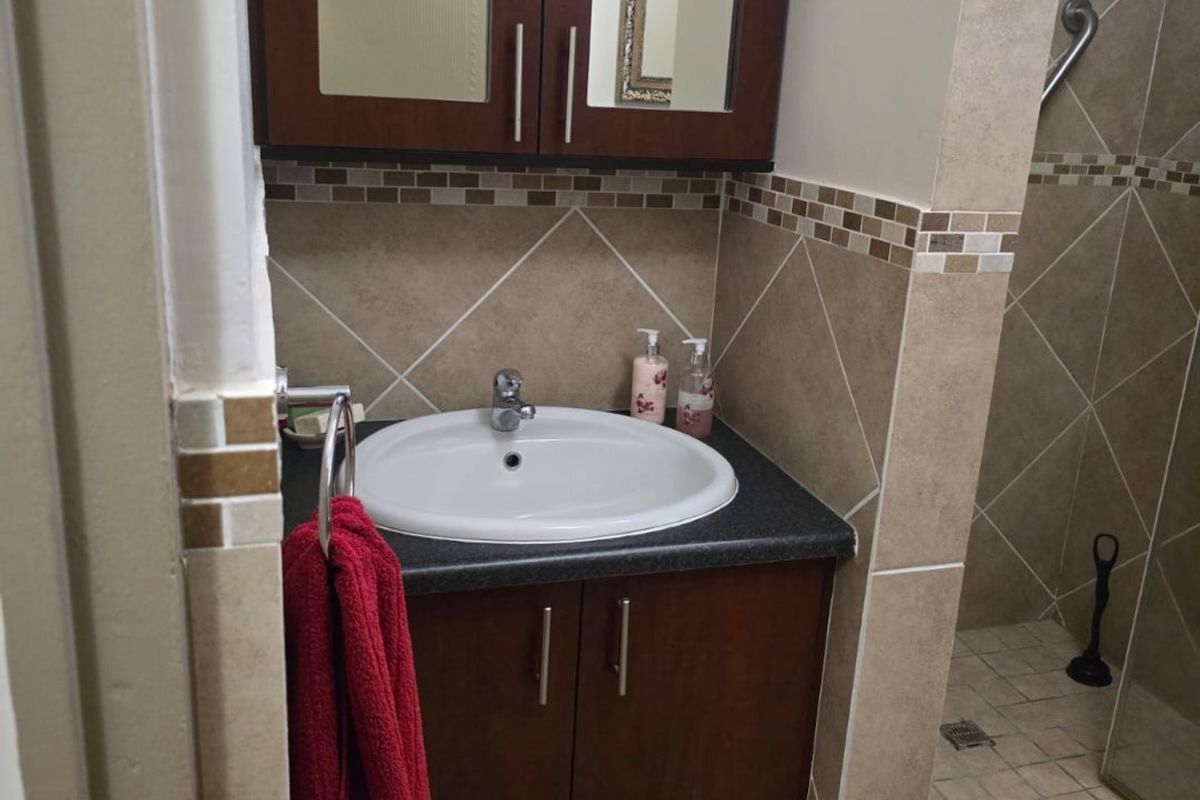 A compact bathroom featuring a dark wood vanity with basin, mirrored medicine cabinet, and a tiled shower enclosure with a grab rail.