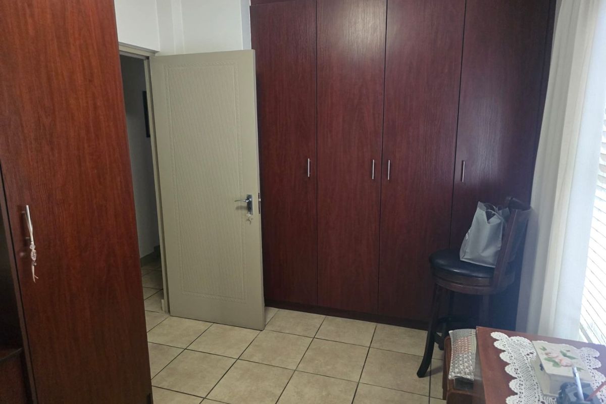 A bedroom featuring dark wood built-in cupboards and neutral tiled flooring, providing functional storage space.