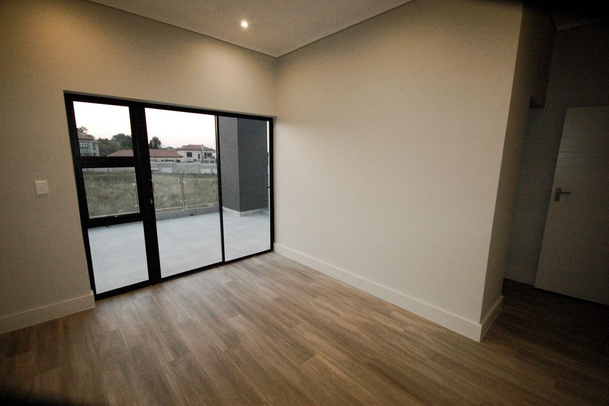A bright, modern, and empty bedroom featuring wood-look laminate flooring, neutral walls, and a large sliding glass door leading to an outdoor balcony.