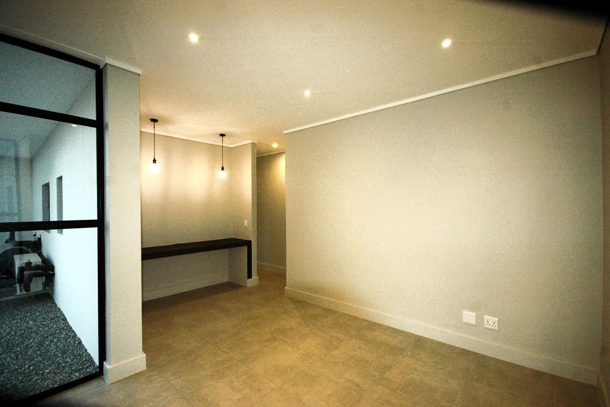 A modern, minimalist living space featuring tiled flooring, recessed lighting, and a sleek black metal framed glass partition.