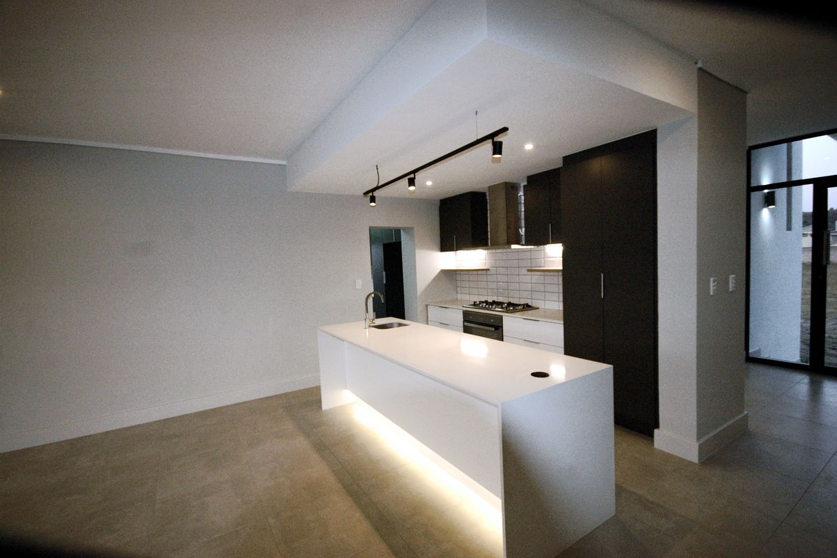 Modern kitchen featuring a central island with integrated sink, sleek dark cabinetry, built-in appliances, and ambient under-cabinet and island lighting.