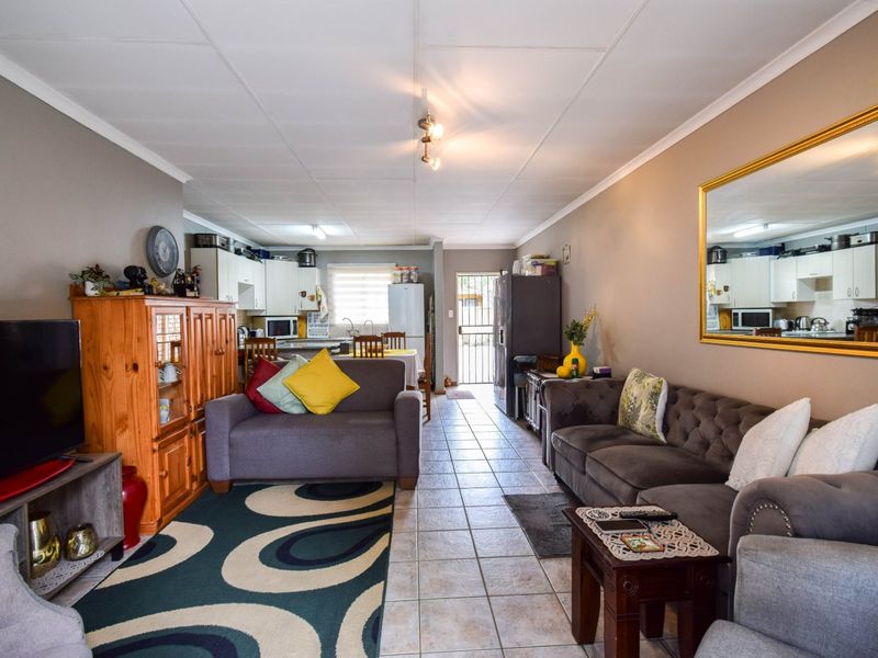 Open-plan living and kitchen area featuring tiled flooring, neutral wall tones, and direct access to the exterior via a security gate.