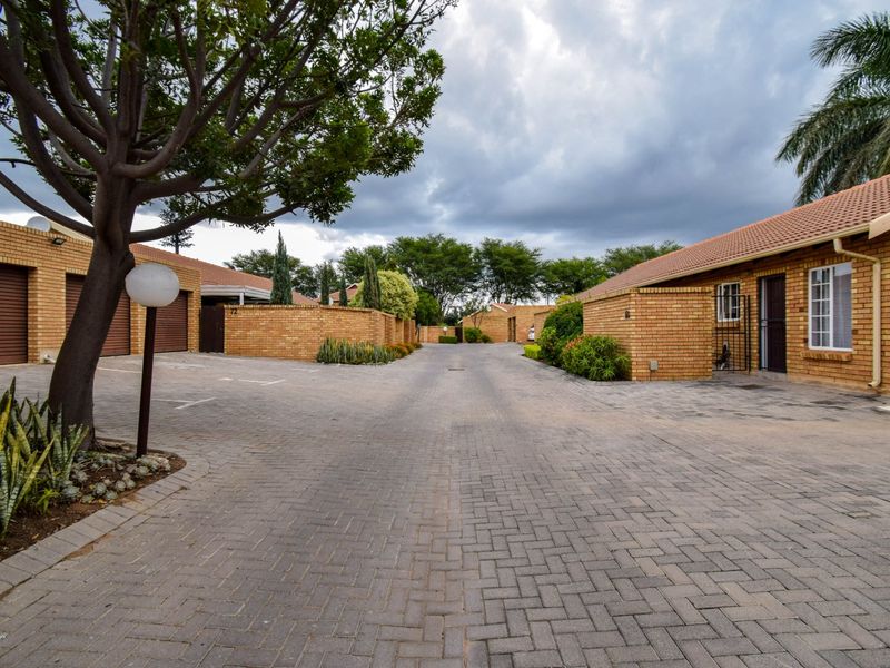 A view of the townhouse complex driveway featuring facebrick facades, tiled roofs, and paved access leading to multiple garage units.