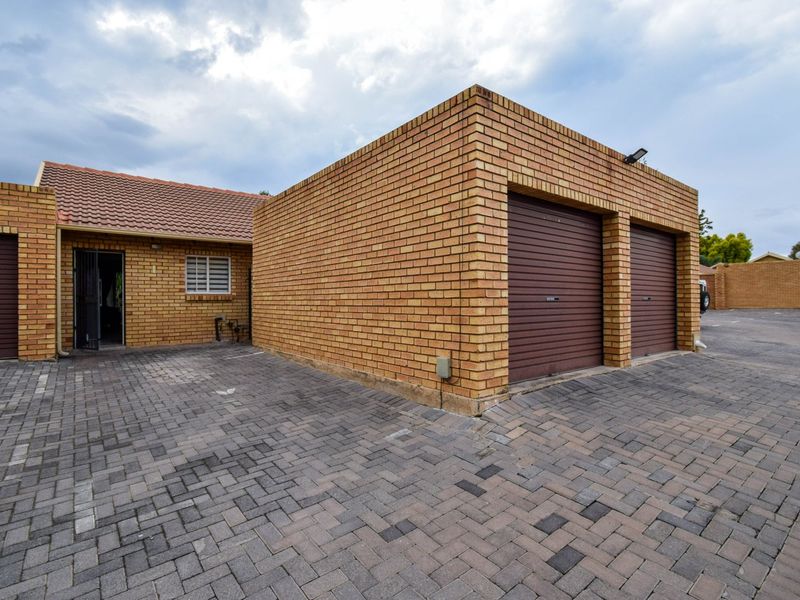 Exterior view of a townhouse featuring a double garage with roller doors, brick facade, and a paved driveway area.