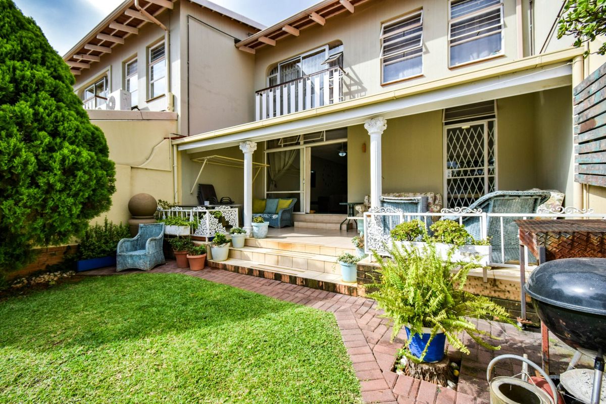 Rear view of the townhouse featuring a covered patio with decorative columns, tiled flooring, and a small balcony above, overlooking a neat garden.