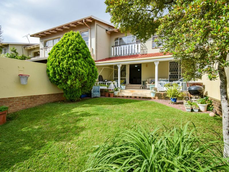 Rear view of the townhouse featuring a private garden, a covered patio area, and an upper-level balcony with a tiled roof.