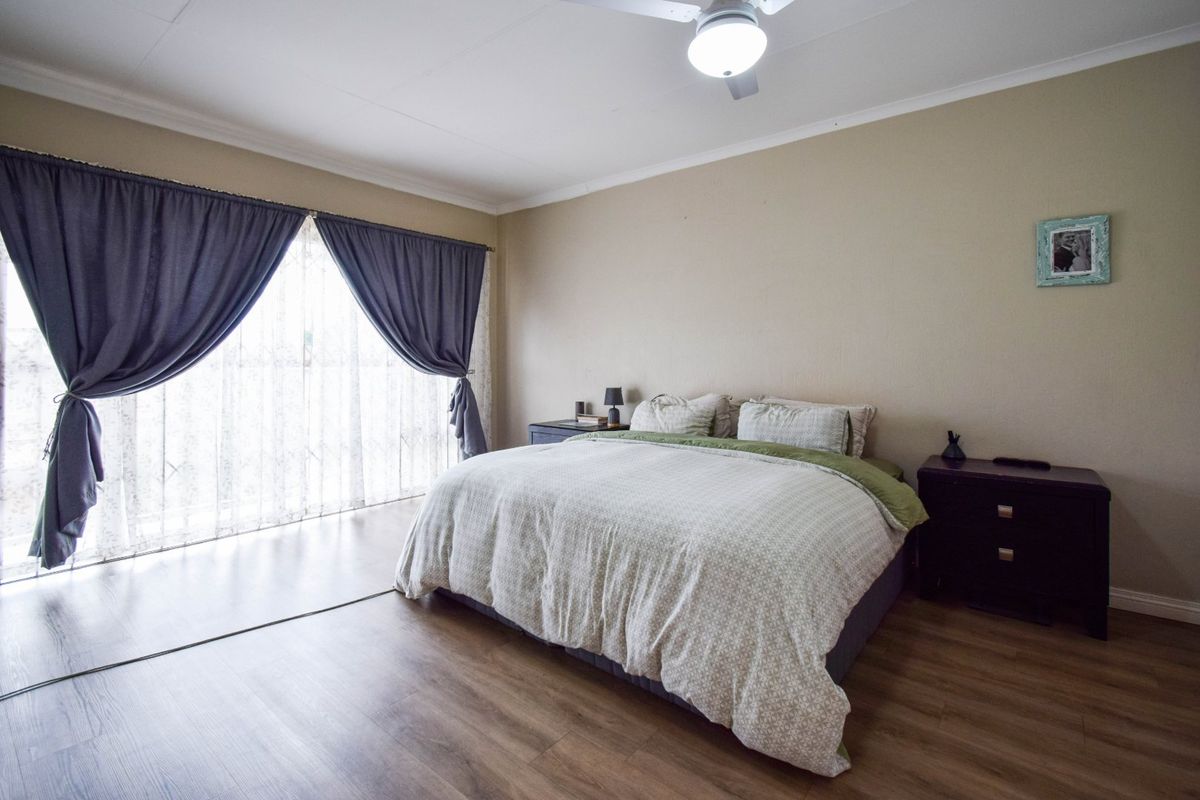 A spacious bedroom featuring laminate flooring, a ceiling fan, and a large sliding glass door providing natural light.