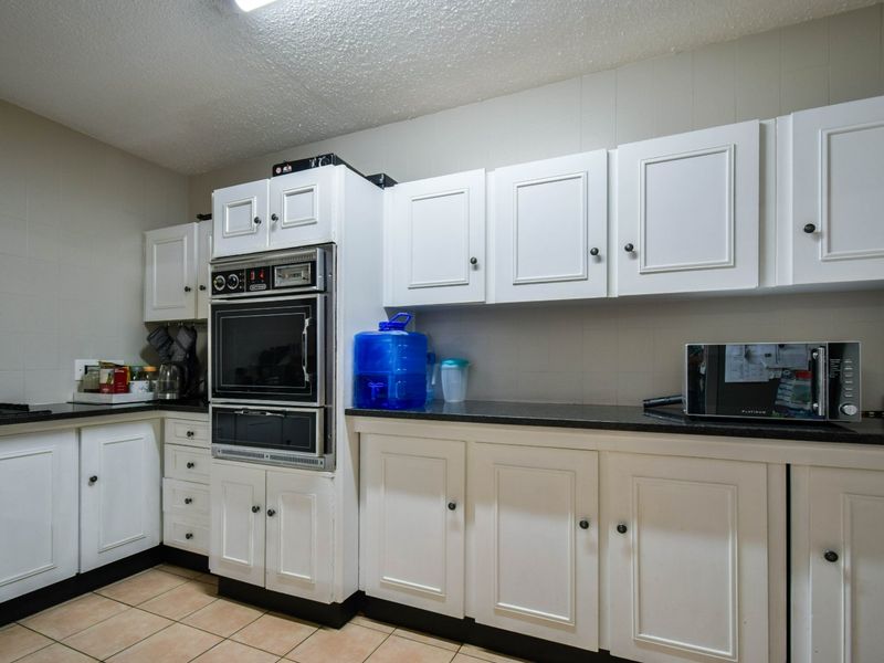 A functional kitchen featuring white cabinetry, dark stone countertops, and ceramic floor tiles, offering a classic layout with integrated oven and ample storage space.