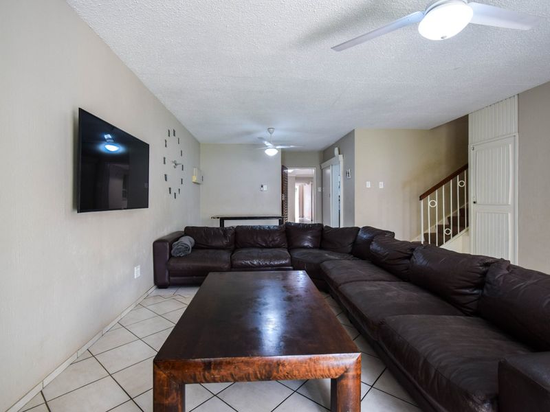 Spacious living area featuring tiled flooring, ceiling fans, and a staircase leading to the upper level.