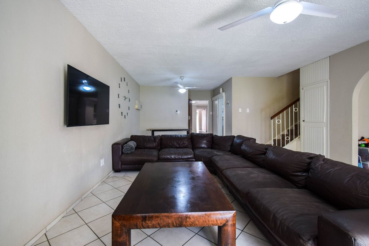 Spacious living area featuring tiled flooring, ceiling fans, and a staircase leading to the upper level.
