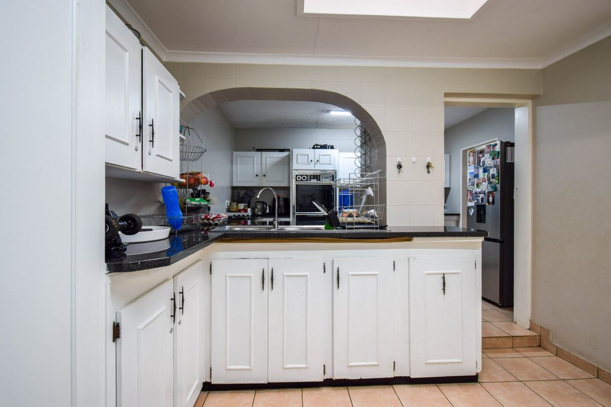 A functional kitchen featuring white cabinetry, granite countertops, and a built-in oven, connected to an adjacent space via a classic architectural archway.